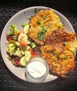 Potato fritters served with sour cream, herbs and salad of fresh seasonal vegetables closeup.