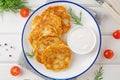 Potato pancakes, latkes or draniki with fresh herbs and sour cream on a plate on a white wooden background. Top view, copy space