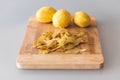 Potato peelings with potatoes on wooden cutting board on grey background