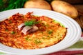 Potato rosti with dill and salted herring in plate on wooden table.