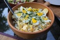 Potato salad with cooked eggs and herbs garnish in a rustic bowl on a glass garden table