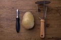 A potatoe with a tool to crushed potatoe and a peeler in the center of a wooden table Royalty Free Stock Photo