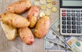 Potatoes, dollars, calculator and coins on a wooden table. View from above.