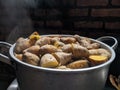 Potatoes with their skins in a stainless steel pot. ripe yam, visible smoke.