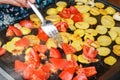 Potatoes and tomatoes cut to small pieces grilled on electric grill, blurred hand holding steel fork moving smoking