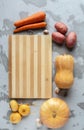 Potatoes, turnips, carrots, pumpkin, and garlic are laid out on a bamboo cutting Board on a gray textured background