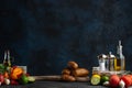 Potatoes on the wooden board with some fruits, vegetables, cutlery and spices isolated on dark blue background. Cooking at home.