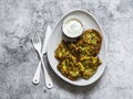 Potatoes, zucchini, herbs fritters with sour cream sauce on a gray background, top view. Delicious breakfast, appetizer, tapas