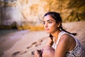 Potrait latin girl sitting on golden sand at beach near rocks and looking at ocean. Summer vocation Royalty Free Stock Photo