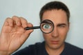 Potrait of a man holding magnifying glass and looking through it srewing up one eye. Funny view to magnified man's glass