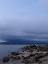 Potrait of a rocky beach with calm water and cloudy mountain