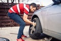 Potrait of young man changing seasonal tires, installing summer tires on automobile