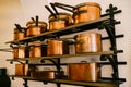 Pots, ladles, tray and saucepan made of copper, in various sizes, on massive metal shelves, fixed to a white wall.