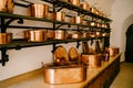 Pots and saucepans in gold-colored copper in various sizes on shelves in a room with a long wooden table