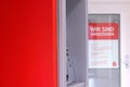 Potsdam, Germany - February 17, 2024: bright red wall, seeing part of grey ATM machine and blurred poster on door with Royalty Free Stock Photo