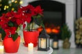 Potted poinsettias, burning candles and festive decor on white table in room, space for text. Christmas traditional flower