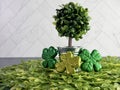 Potted tree sitting on a bed of green leaves with 3 four leaf clovers covered in glitter, against a herringbone tile for St.