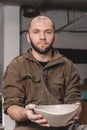 Potter holding a plate that was made of white clay on the potter`s wheel circle in studio, concept of creativity and art, vertica