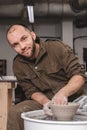 Potter making a bowl of white clay on the potter`s wheel circle in studio, man looking at the camera and smiling, concept of