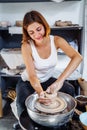Potter woman, sculptor, with a sculpting tool, creatively shapes a piece of wet clay with a potter`s wheel. Professional workshop