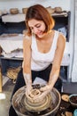 Potter woman, sculptor, with a sculpting tool, creatively shapes a piece of wet clay with a potter`s wheel. Professional workshop