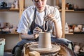 Potter working on a Potter`s wheel making a vase. Young woman forming the clay with hands creating jug in a workshop