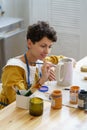 Young smiling creative woman working in her own cozy pottery studio, making ornament on ceramic jug