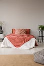 Pouf on carpet in minimal grey bedroom interior with red bed with pillows between plants