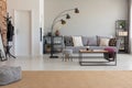 Pouf on carpet in spacious flat interior with lamp next to grey sofa and wooden table