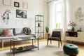 Pouf next to armchair in living room interior with table in front of sofa under posters. Real photo Royalty Free Stock Photo