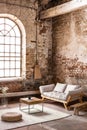 Pouf and table on rug in front of wooden sofa in spacious loft interior with window