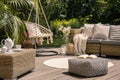 Pouf on wooden terrace with rattan sofa and table in the garden with hanging chair. Real photo Royalty Free Stock Photo