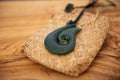Pounamu fish hook necklace on grainy wooden background. Aotearoa, New Zealand, Maori. Side angle view. Royalty Free Stock Photo
