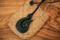 Pounamu fish hook necklace on grainy wooden background. Aotearoa, New Zealand, Maori. Side angle view.