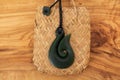 Pounamu fish hook necklace on grainy wooden background. Aotearoa, New Zealand, Maori. Top view.