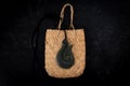 Pounamu fish hook necklace on weaved bag on dark background. Aotearoa, New Zealand, Maori.