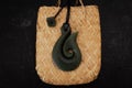 Pounamu fish hook necklace on weaved flax bag on dark background. Aotearoa, New Zealand, Maori. Royalty Free Stock Photo