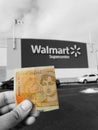 Pound currency note in hand in front of Walmart supermarket sign