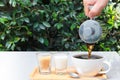 Pour coffee into a cup on a wooden tray with milk and sugar next to it. Tables are located in the restaurant, garden setting. Royalty Free Stock Photo