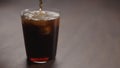 pour cola over ice cubes into tumbler glass on walnut table with copy space Royalty Free Stock Photo