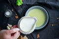 Pour cream into cream soup. Close-up. Milk jug with cream in female hands.