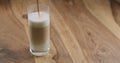 Pour espresso into steamed milk into glass on wood table