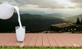 Pour fresh milk from the jug into a clear glass and place it on a wooden plank. Drink for breakfast. The mountain background in Royalty Free Stock Photo