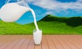 Pour fresh milk from the jug into a clear milk glass placed on a wooden plank floor. There is a little shadow. Bright green meadow Royalty Free Stock Photo