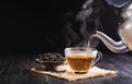 Pour the hot herbal teapot into a glass cup. Teacup is placed on a black wooden table on dark background. The sunlight of the new