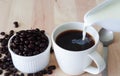 Pour milk into coffee cup that set on wood table and coffee beans placed at side. Royalty Free Stock Photo