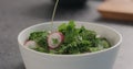 Pour olive oil into fresh salad with radish, cucumber and herbs in white bowl Royalty Free Stock Photo