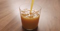 Pour orange juice in thin wall glass on wood table