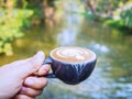 Pour out coffee late cup in hand, with green nature and canal background. coffee lover Royalty Free Stock Photo
