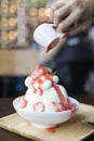 Pour strawberry sauce on shaved ice topping with strawberry slice and cream.